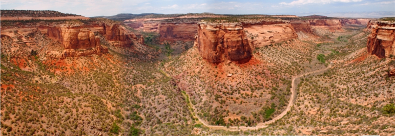 [Several photos stitched together showing a canyon coming down from the left side and then going around a bend in front before continuing away to the right. There is a huge 'tabletop' in the middle of the image around which a road/river wends.]